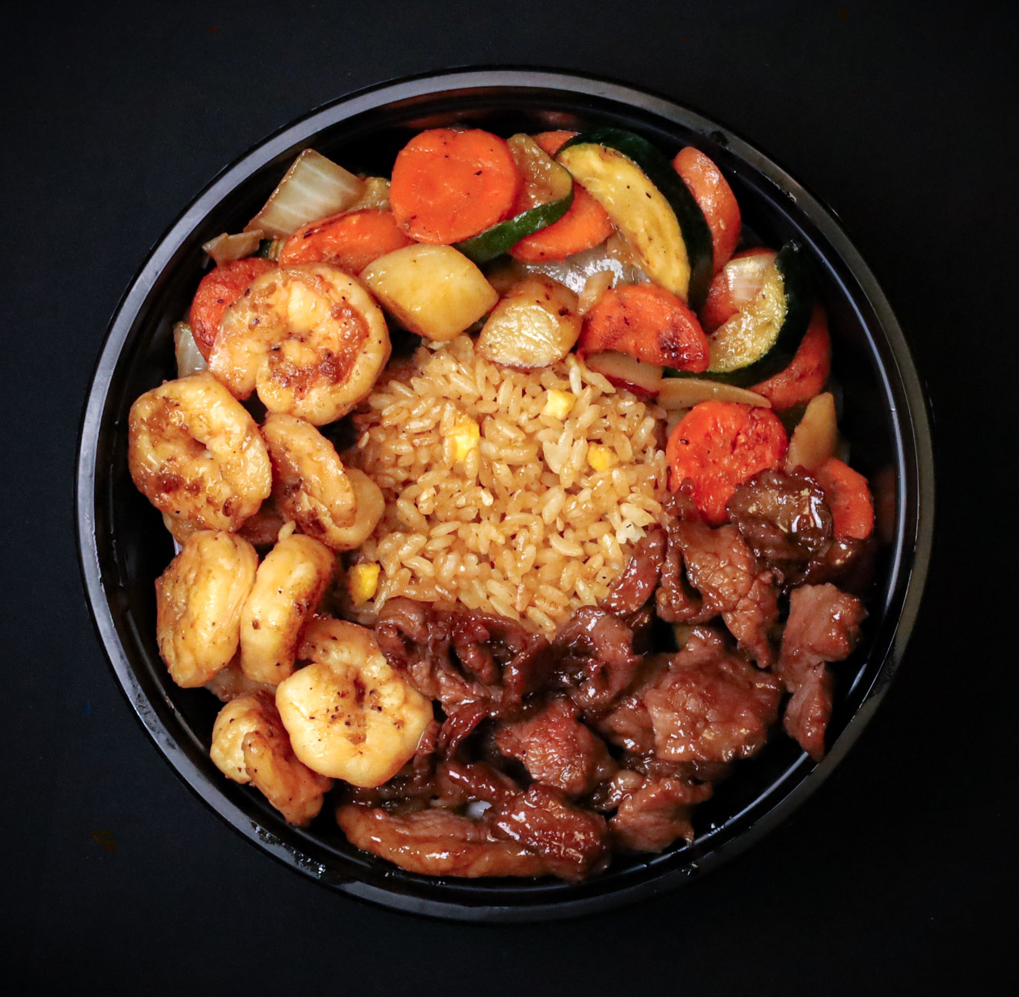 A shrimp and steak hibachi bowl with fried rice and vegetables